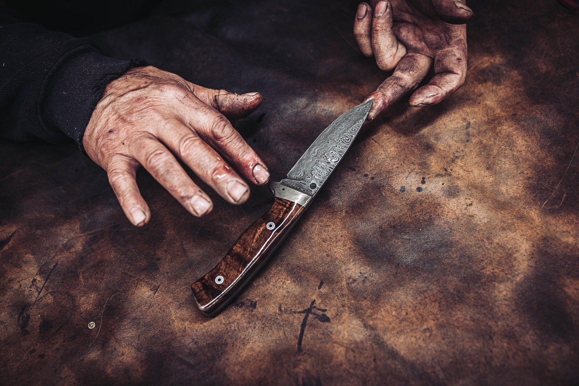 Rußige Hände und fertiges Damastmesser auf Leder